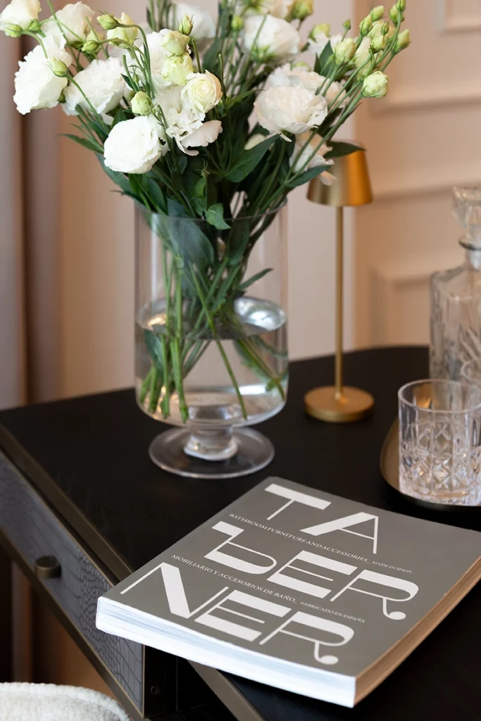 Minimalist tabletop vignette with gold lamp, glassware, Taberner Spain design book of bathrooms, and clean architectural styling.