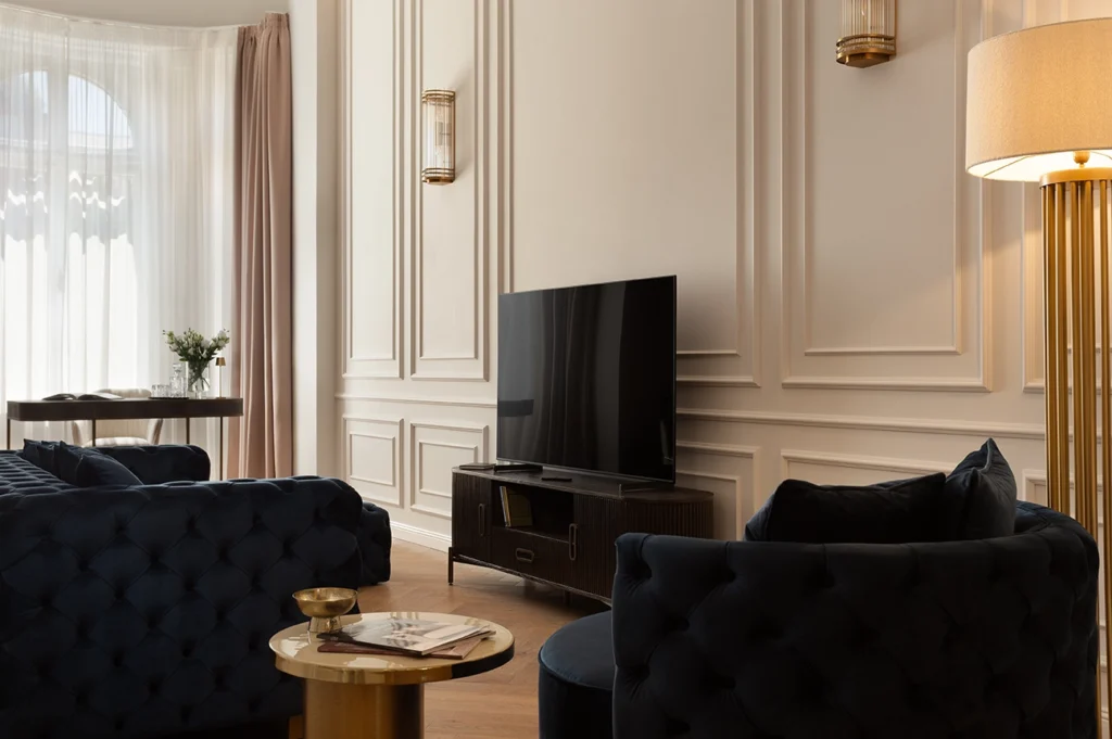 Living room with tufted velvet sofas, gold accent side table, paneled cream walls, designer media console, and sculptural floor lamp.