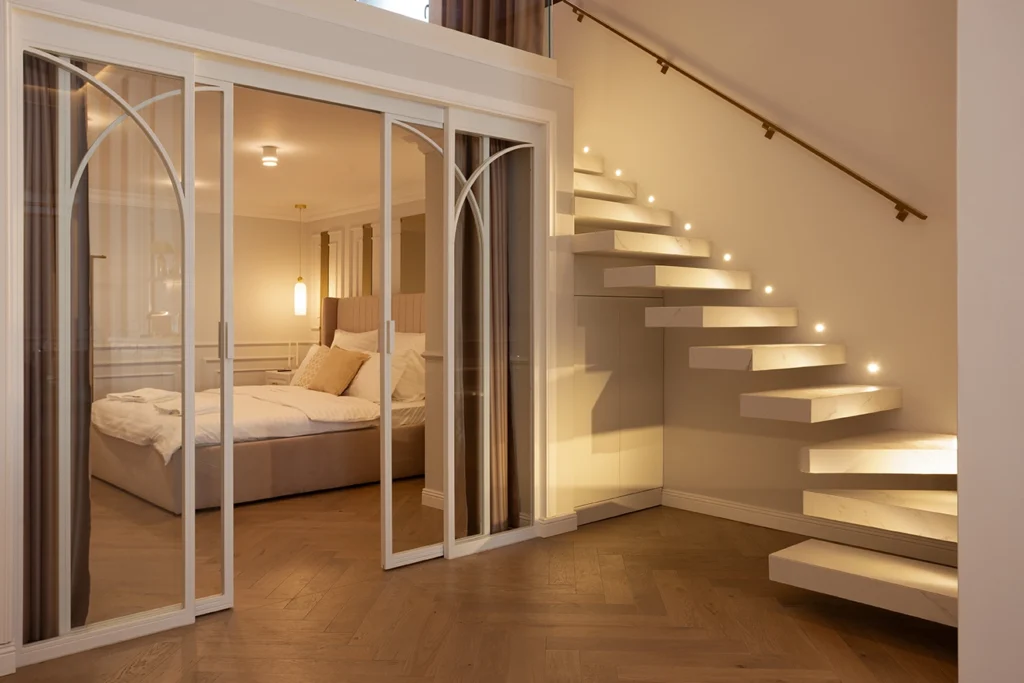 Floating staircase with built-in step lighting, arched glass partition, herringbone wood flooring, and minimalist bedroom styling.