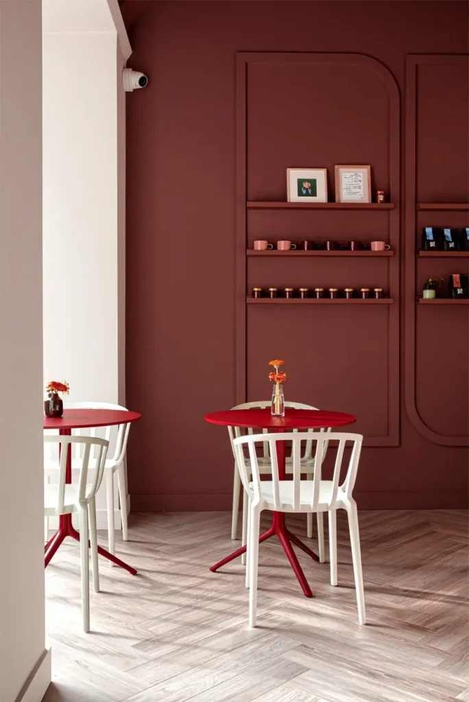 Fotografie de interior minimalist realizată la Bonjour by Lolita de fotograf de design interior și arhitectură – cafenea modernă cu pereți burgundy, mobilier alb și roșu, decor elegant cu flori portocalii, ideală pentru promovarea spațiilor comerciale