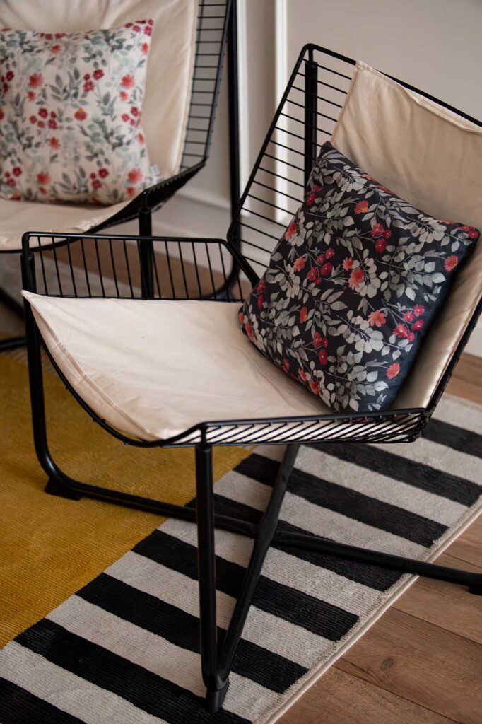 Ilisie Sergiu photograph with a close‑up of a modern hospitality lounge bertoia chair with black metal frame and beige upholstery, styled with floral cushions in contrasting tones and placed over striped and mustard rugs, a refined detail that conveys warmth, texture, and boutique character in hotel or apartment interiors.