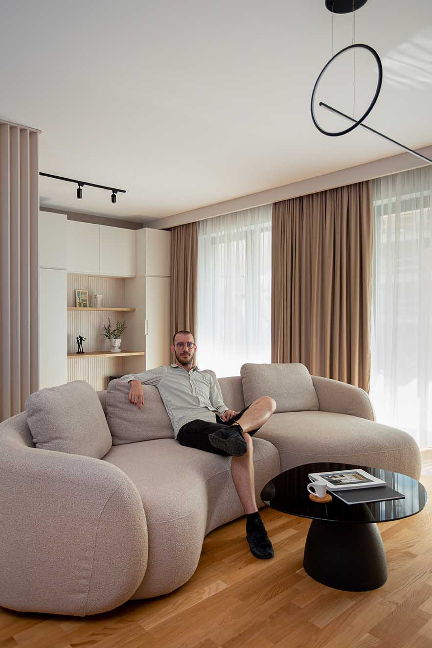Contemporary living area detail featuring a sculptural beige boucle sofa and a black glass coffee table with minimalist styling. A refined composition that appeals to interior designers focused on tactile materials, neutral palettes, and modern spatial balance.